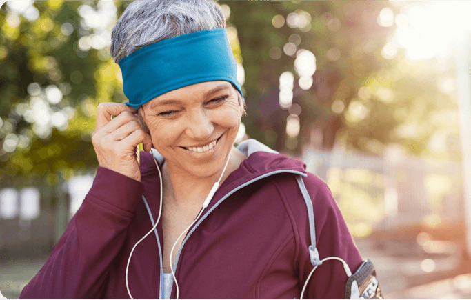 An elderly woman wearing earbuds and a headband, focused and enjoying her music while jogging